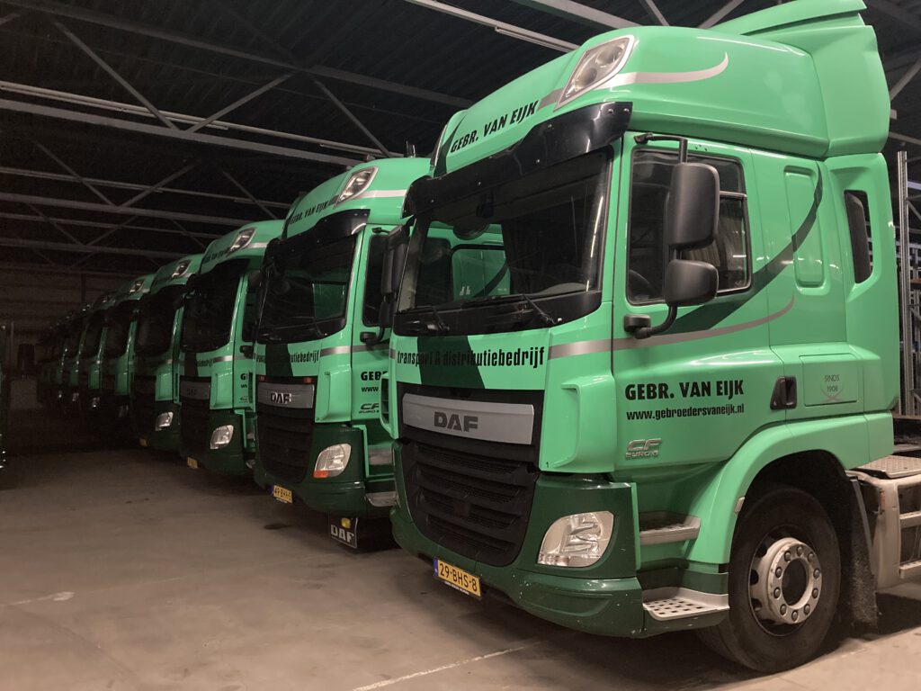 Groene vrachtwagens van Gebr. Van Eijk Transport en Distributiebedrijf geparkeerd in een opslagruimte.